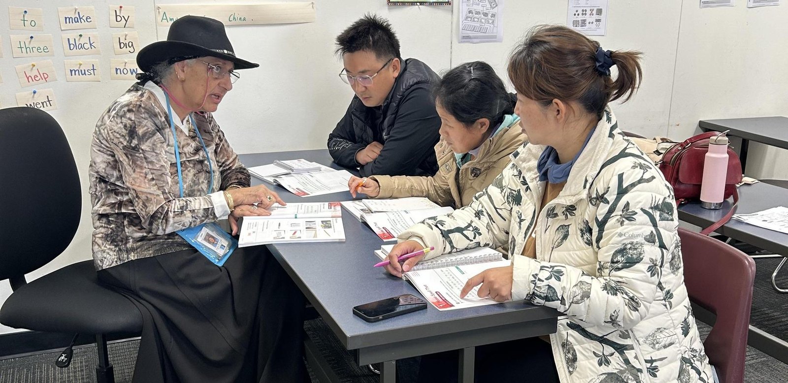 教师为三名成年学员辅导英语阅读与练习